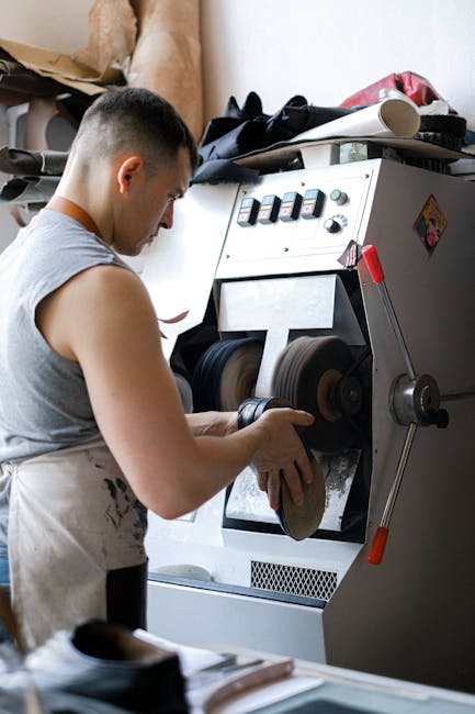 Leather artisan sanding shoes using industrial machine. Focus on craftsmanship and detail.