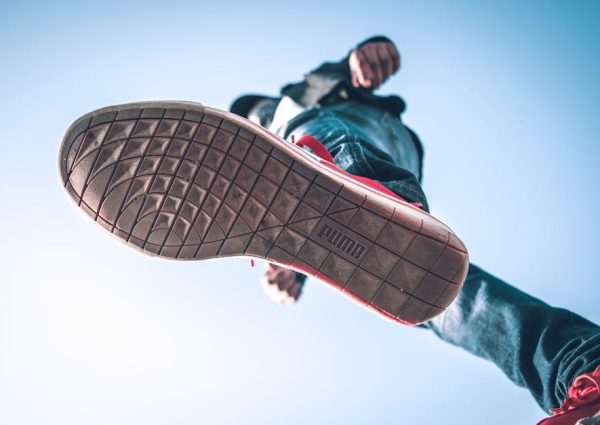 Low angle view of person wearing sneakers with focus on the sole against blue sky.
