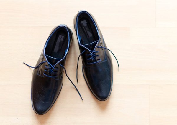 Pair of stylish black leather shoes with blue laces on a wooden floor.