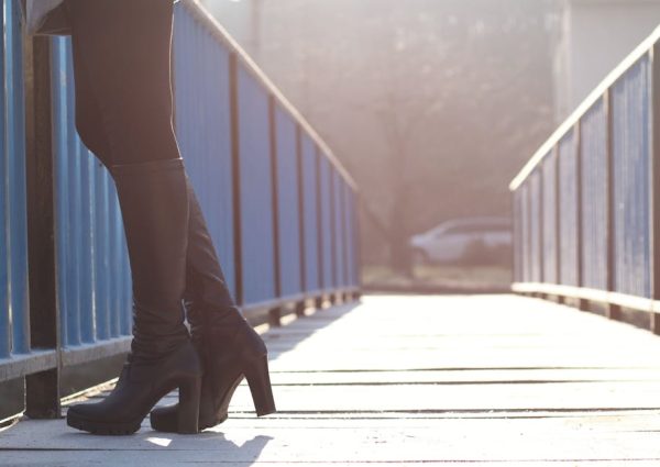 Close-up of a woman's black boots on a sunny urban bridge, capturing a modern city vibe.